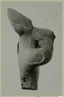 Terracotta figurine fragment of a torso with one arm bent across the chest, head missing, against a plain background.