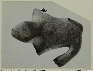 Terracotta figurine of an animal with a blunt head and one leg extended downward, shown as a mounted print.