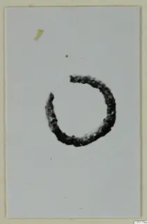 Dark, open ring-shaped find photographed on a pale card, from Ayios Iakovos Tomb 8.