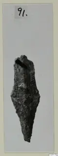 Corroded metal object tapering to a point, with a dark cavity at the upper end, from Ayios Iakovos Tomb 8