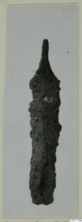 Corroded metal object from Ayios Iakovos Tomb 8, photographed against a pale grey background