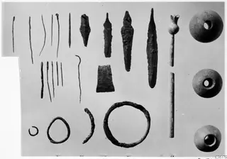 Bronze tools, weapons and small finds from Ayios Iakovos Tomb 8, laid out in rows on a plain ground
