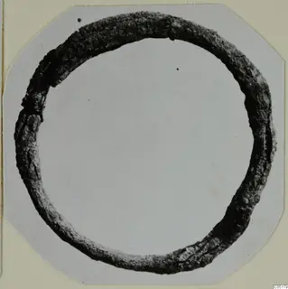 Dark, corroded ring from Ayios Iakovos Tomb 8, shown on a grey card mount