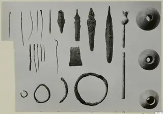 Bronze tools, weapons and small finds from Ayios Iakovos Tomb 8, laid out in rows on a grey background