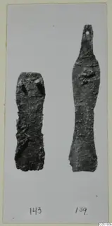 Two corroded metal objects side by side on a card, the right one with a small hole at its top end.