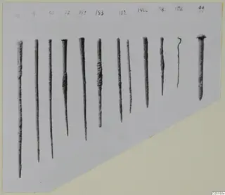 About a dozen corroded metal pins and tools in a row, each with a handwritten number label above it.