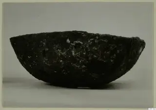 Dark, rough-surfaced bowl seen from the side against a grey backdrop