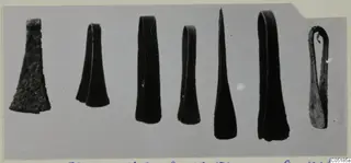 Seven bronze objects from Lapithos Tomb 320 laid in a row on a pale grey background