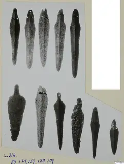 Eleven bronze tools arranged in two rows, long and pointed, some with rivet holes at the upper end, on a card mount