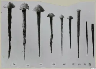 Nine corroded metal pins with conical heads, set in a row with number labels beneath them