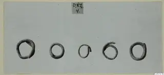 Five dark ring-shaped objects in a row on a grey card, from Lapithos Tomb 316