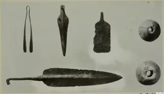 Bronze tools, a spearhead and two perforated beads laid out on a grey background, finds from Lapithos Tomb 302A
