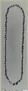 Necklace of small rounded beads laid out in a long oval loop on a plain grey background, from Lapithos Tomb 313 B