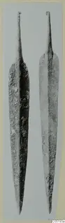 Two long, pointed bronze blades with narrow stems, photographed upright side by side, from Lapithos Tomb 315 B-C