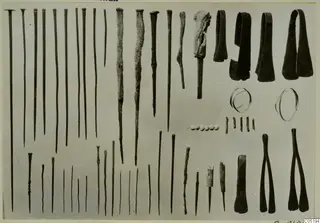 Group of metal pins, tongs, rings and beads from Lapithos Tomb 313 A, arranged on a pale background