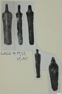 Five dark, corroded bronze objects with narrow stems and flat blades, cut-out photographs mounted on a card