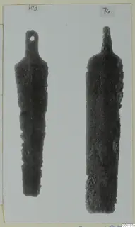 Two bronze tools with long tapering blades and narrow tangs, photographed on a mounted card.