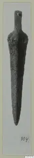 Corroded metal tool with a narrow tang at the top and a long tapering point, shown on a photo mount.