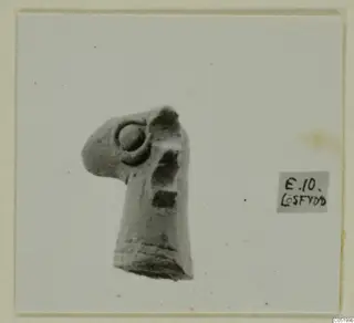 Fragment of a small pale clay figure with a ring-shaped boss and ridged base, shown on a mounted card.