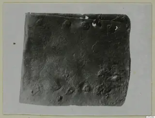 Corroded dark metal plate with raised knobs from Lapithos Tomb 409