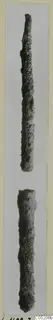 Two long, corroded metal objects shown one above the other, the upper one tapering to a point.