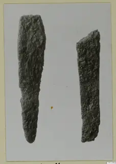 Two corroded metal objects from Lapithos Tomb 409, one long and tapering to a point, the other a short flat bar