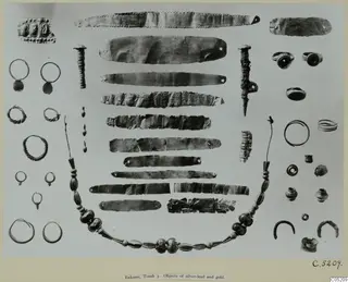 Gold and silver objects from Enkomi, Tomb 3, including jewellery and flat strips, laid out on a pale grey background