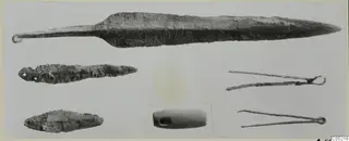 Bronze blades, two bronze tongs and a perforated stone object from Ayios Iakovos Tomb 10 A, laid out on a pale background.