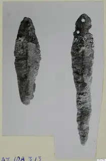 Two corroded metal tools or weapons from Ayios Iakovos Tomb 10 A, one with two small holes near its top end.