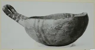 Pottery bowl with a long strap handle and dark painted bands, photographed against a plain background.