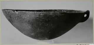Pottery Black Slip Ware bowl with a small pierced handle at one end, shown in side view