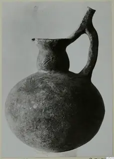 Round-bodied pottery jug with a strap handle and incised lines on neck and shoulder, dark surface