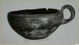 Black polished cup with a large loop handle and pale incised zigzag and banded decoration