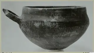 Pottery Monochrome Ware bowl with a single loop handle, photographed from the side against a plain grey background