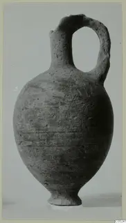 Pottery jug with a single loop handle, Black Lustrous Ware, shown upright against a plain grey background.