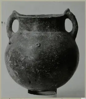 Round-bodied pottery vessel with two loop handles and a dark slipped surface, shown on a small stand.