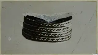 Banded metal object with diagonal chevron pattern, shown centred on a grey card, from Enkomi