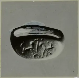 Finger ring with an oval bezel carrying raised engraved motifs, photographed at an angle on grey card, Enkomi.