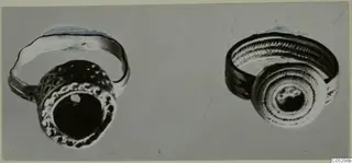 Two finger rings with dark central stones, shown side by side on a grey background