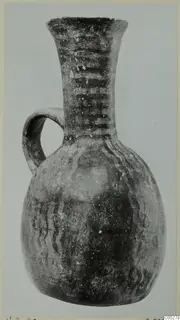 Pottery jug with a single loop handle, flaring neck and dark painted bands, photographed against a plain grey background