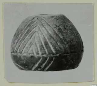 Rounded object with incised chevron lines above a raised horizontal ridge, shown in a close photograph.