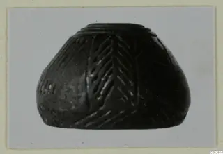Small dark vessel with a stepped rim and incised chevron pattern on its body