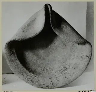 Terracotta bowl-shaped object with a pinched rim rising into three raised lobes, photographed on a light surface.