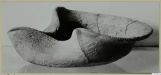 Terracotta lamp in side view, with two raised pinched ends and cracks across the body