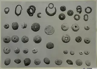 Grid of small bronze jewellery parts from Arsos: wire rings, a crescent-shaped piece and ribbed, perforated beads.