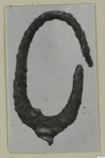 Corroded metal open-ended loop, likely a bronze piece of jewellery, from Arsos, photographed on a grey card.
