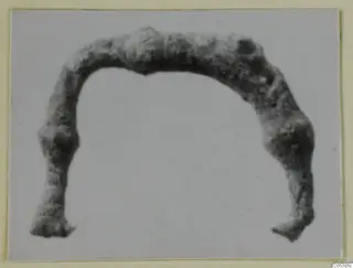 Bronze fibula from Lapithos, a corroded arched bow with flattened ends, photographed on a pale background