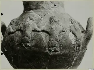 Close view of the body of a large pottery vessel with applied relief figures and cracks across the surface