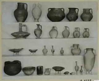 Pottery vessels from Tomb 9 at Marion, arranged in four rows on shelves against a light backdrop.