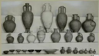 Pottery from Marion, Tomb 22: tall amphorae, jugs and small bowls arranged in rows on a light backdrop.